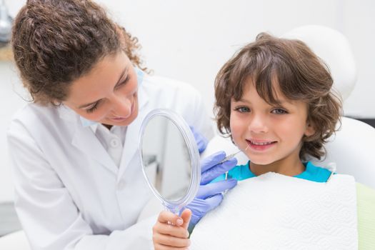 Pediatric dentist showing little boy his teeth in the mirror at the dental clinic