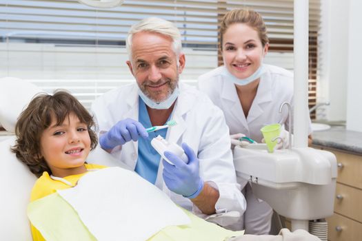 Pediatric dentist showing little boy how to brush his teeth at the dental clinic