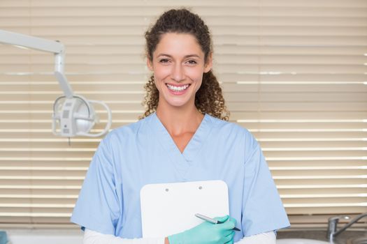 Dentist in blue scrubs holding clipboard at the dental clinic