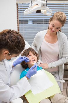 Pediatric dentist examining a little boys teeth with his mother at the dental clinic