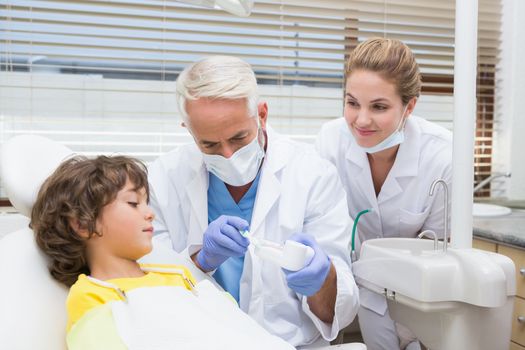 Pediatric dentist showing little boy how to brush his teeth at the dental clinic