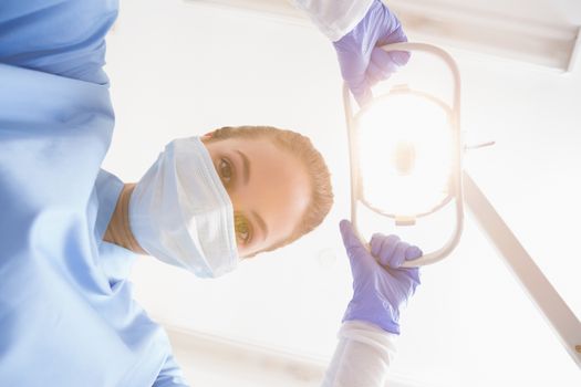 Dentist in surgical mask shining light over patient at the dental clinic