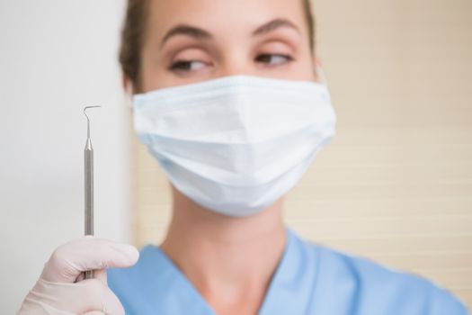 Dentist in surgical mask holding dental explorer at the dental clinic