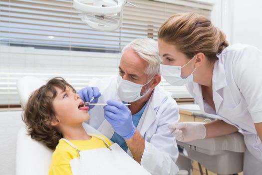 Pediatric dentist examining a little boys teeth with his assistant at the dental clinic