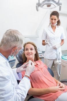 Dentist examining a patients teeth in the dentists chair with assistant at the dental clinic