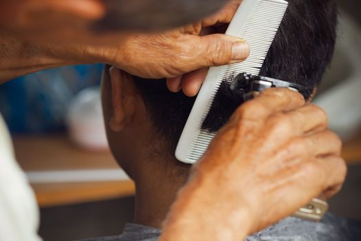 Closeup hand of hairdresser cutting hair with clipper at local barber shop.