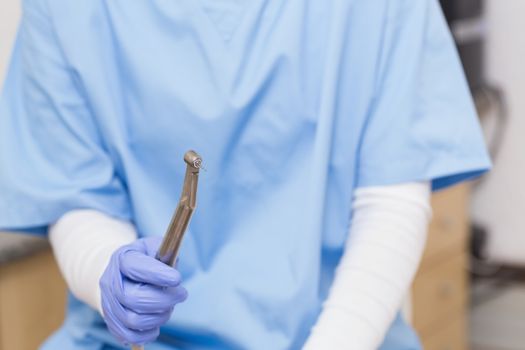 Dentist in blue scrubs holding dental drill at the dental clinic