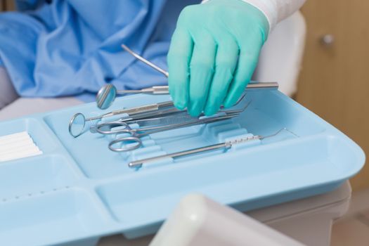 Dentist in blue scrubs picking up tools at the dental clinic