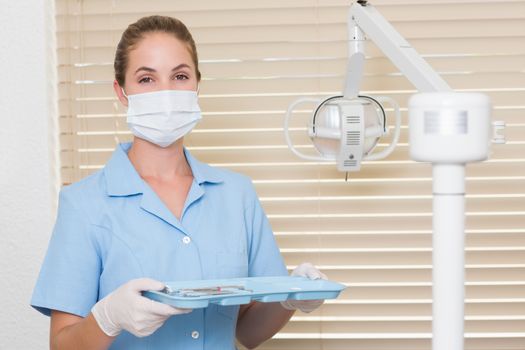 Dental assistant in blue holding tray of tools at the dental clinic