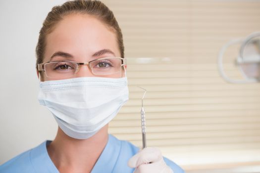 Dentist in surgical mask holding dental explorer at the dental clinic