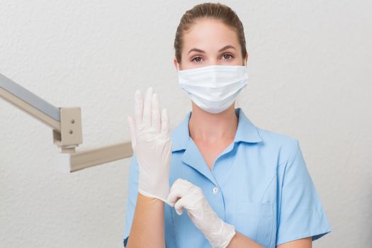 Dental assistant in mask looking at camera pulling on gloves at the dental clinic