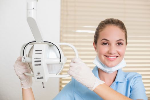 Dental assistant smiling at camera beside light at the dental clinic