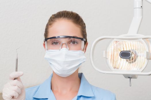 Dental assistant in mask holding dental explorer at the dental clinic