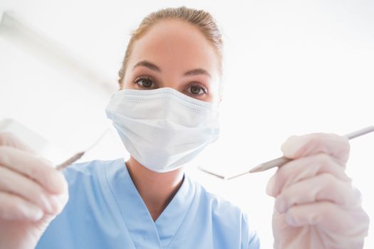 Dentist in surgical mask holding tools over patient at the dental clinic
