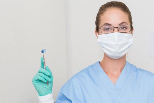 Dentist in blue scrubs holding angled mirror looking at camera at the dental clinic