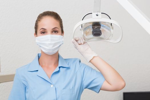 Dental assistant in mask holding light at the dental clinic