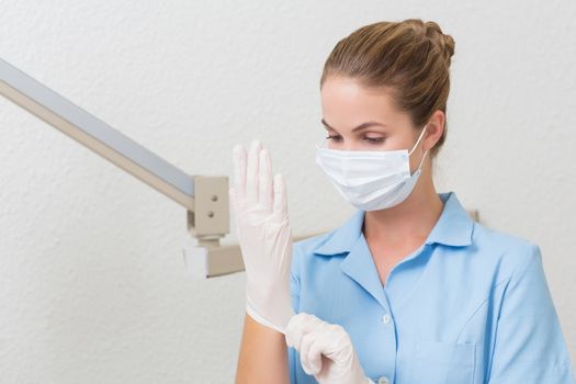 Dental assistant in mask pulling on gloves at the dental clinic