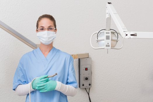 Dentist in blue scrubs holding dental drill looking at camera at the dental clinic