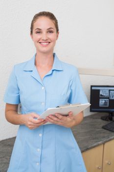 Smiling dental assistant looking at camera holding clipboard at the dental clinic