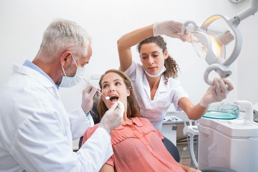 Dentist examining a patients teeth in the dentists chair with assistant at the dental clinic