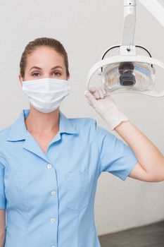 Dental assistant in mask holding light at the dental clinic