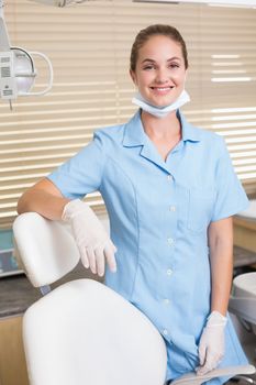 Dental assistant smiling at camera beside chair at the dental clinic