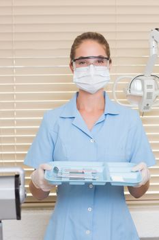 Dental assistant in blue holding tray of tools at the dental clinic