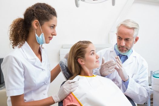 Dentist examining a patients teeth in the dentists chair with assistant at the dental clinic