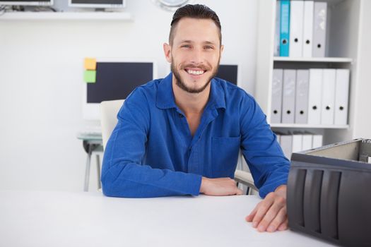Computer engineer sitting at desk smiling at camera in his office