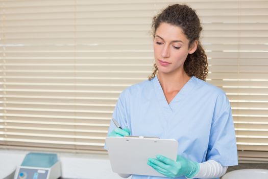 Dentist in blue scrubs writing on clipboard at the dental clinic