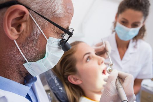 Dentist examining a patients teeth in the dentists chair with assistant at the dental clinic