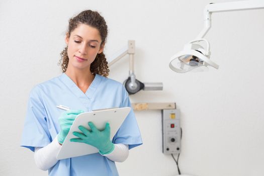 Dentist in blue scrubs writing on clipboard at the dental clinic