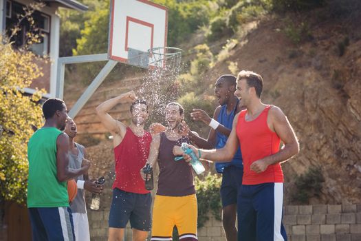 Basketball players celebrating by splashing water on each other in basketball court outdoors