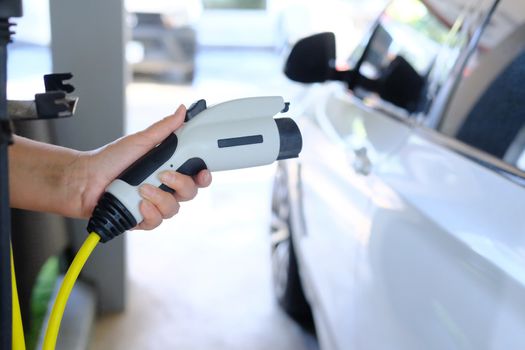 Close up of Human hand holding plug in connector for Charging electric car on electric car background. Concept of an electric car  ecological way of driving.