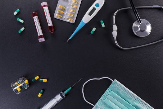 Blood test tube with the Coronavirus disease for virus test and research. Blood test tube with protective masks, medicines, thermometer, stethoscope and syringe on a black background. 