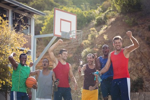 Basketball players celebrating by splashing water on each other in basketball court outdoors