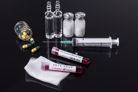 Blood test tube with the Coronavirus disease for virus test and research. Blood test tube with protective masks, medicines, thermometer, stethoscope and syringe on a black background.