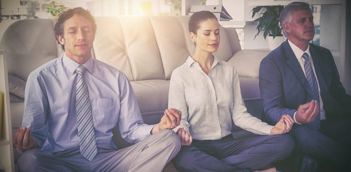 Business people meditating in lotus pose against sofa at office