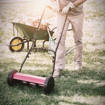 Full length portrait of a smiling man mowing the lawn