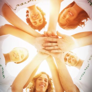 Smiling group of volunteers stacking hands on white background