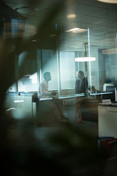 Business people interacting with each other during meeting at office seen through glass