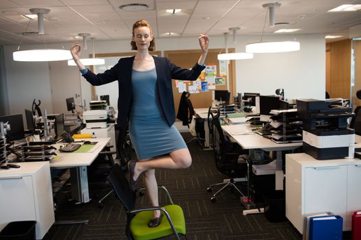 Full length of businesswoman practicing yoga while standing on chair at office