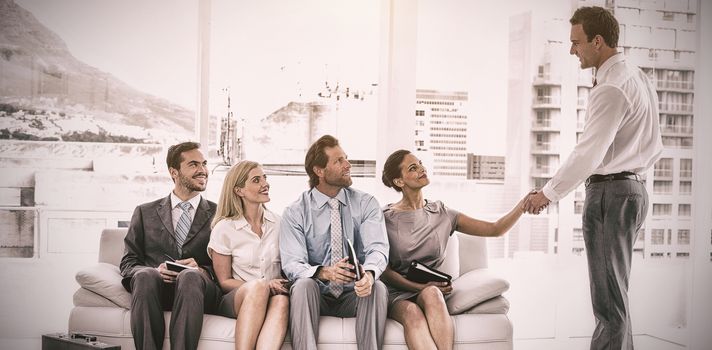 Businessman shaking hand with woman sitting with people waiting for interview in office