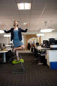 Full length of businesswoman practicing yoga at office