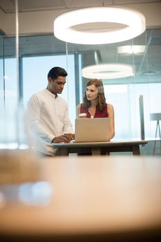 Business people discussing over laptop in illuminated office