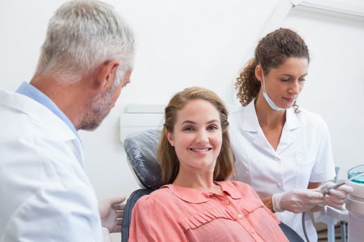 Dentist talking with patient while nurse prepares the tools at the dental clinic