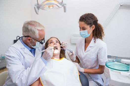 Dentist examining a patients teeth in the dentists chair with assistant at the dental clinic