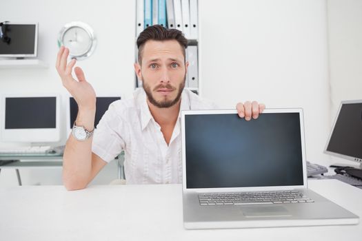 Confused computer engineer looking at camera with laptop in his office