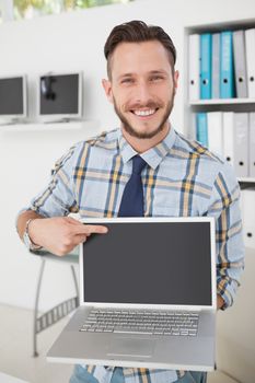 Happy casual businessman pointing to laptop in his office