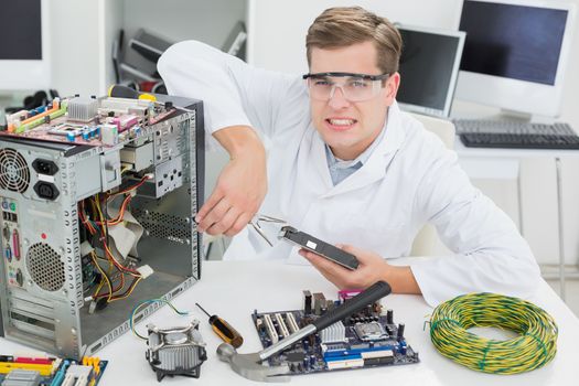 Angry computer engineer working on broken device in his office